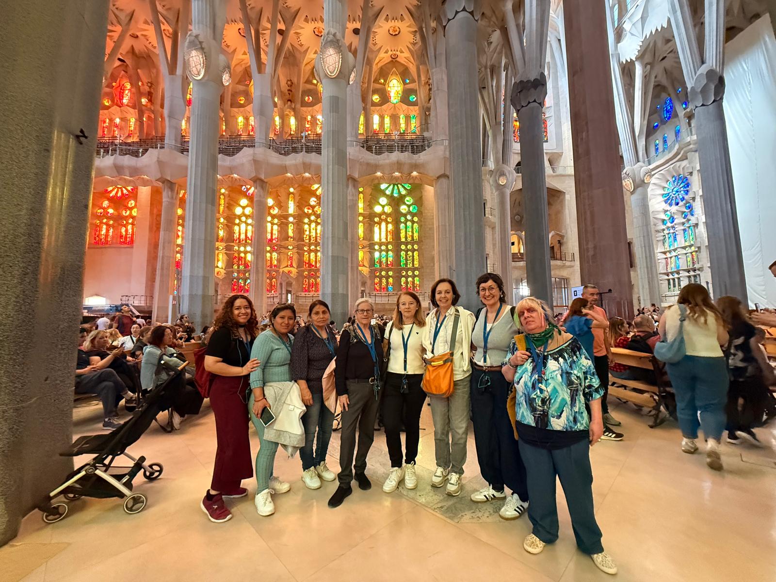 Un grup de 8 dones mira a càmera somrient a l'interior de la basílica de la Sagrada Família de Barcelona. 