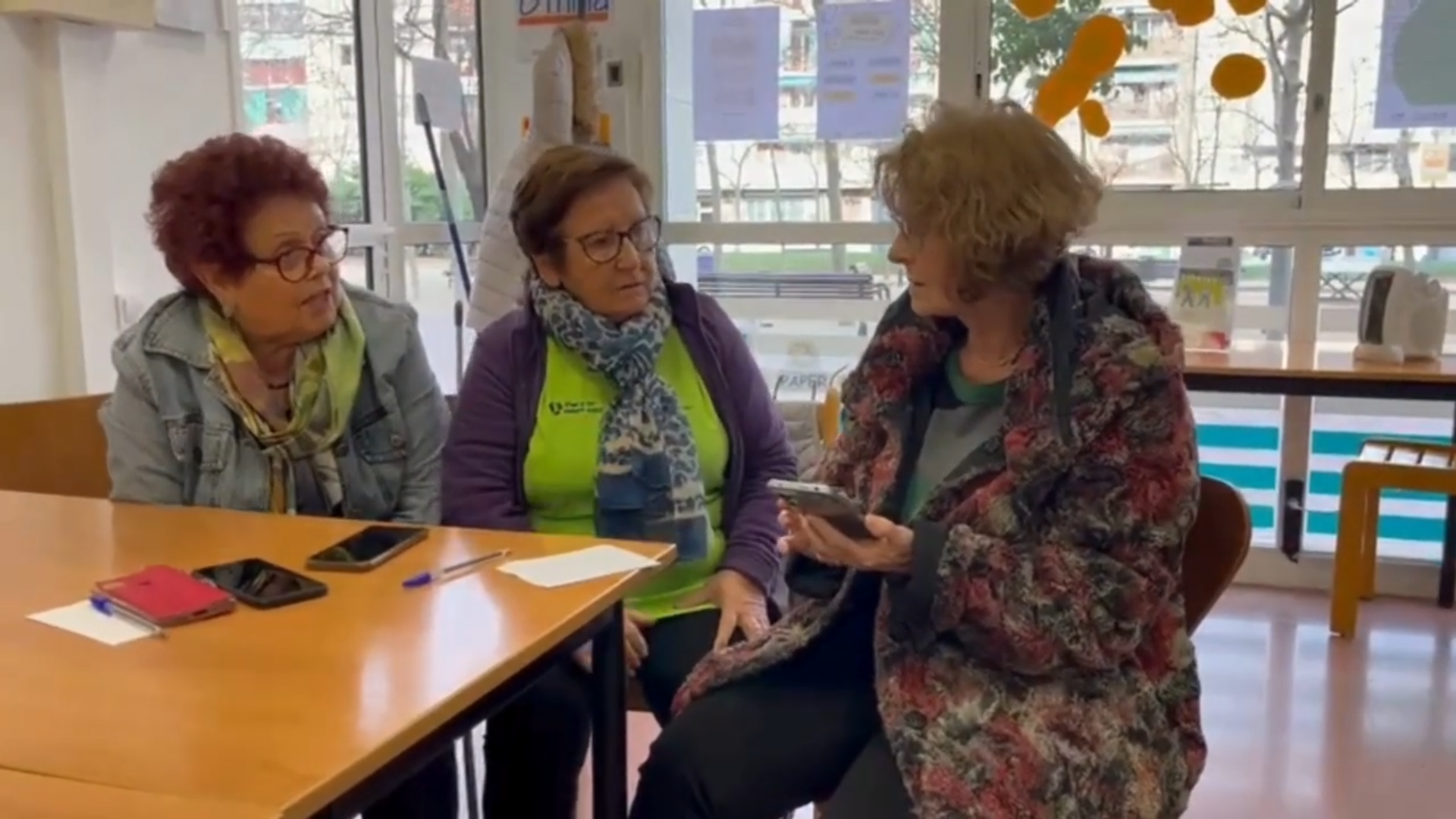 Tres dones grans conversen assegudes davant d'una taula. Cadascuna d'elles té un mòbil.