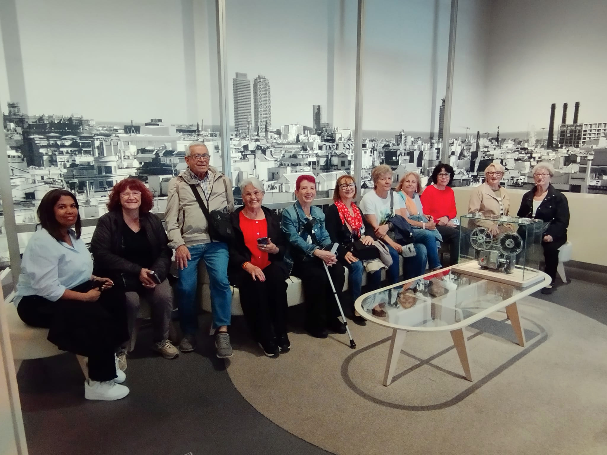 Un grup de 11 persones - del col·lectiu de gent gran - asseguts a un sofà que miren somrinet a càmera. 