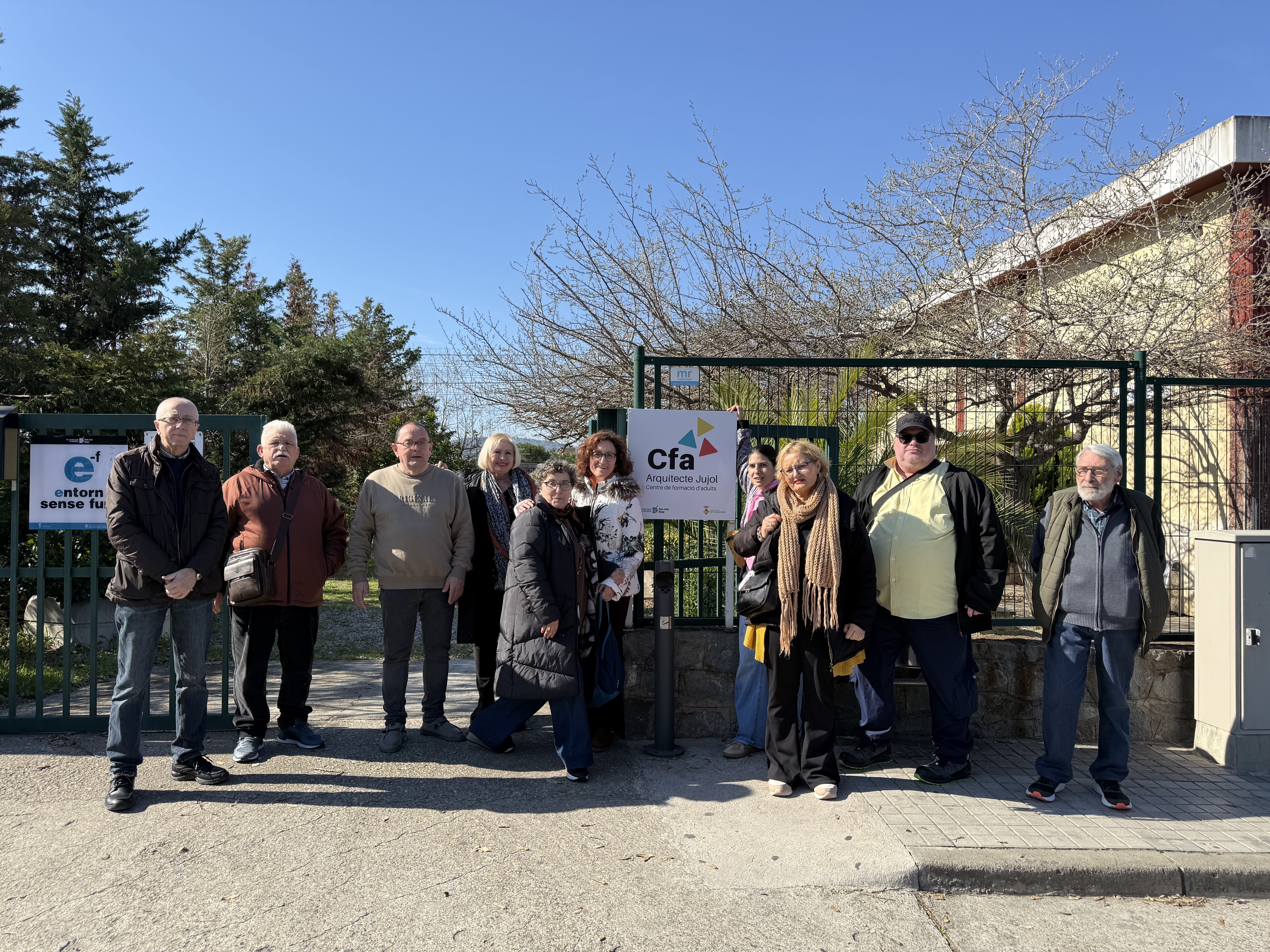 10 participants del Punt Òmnia Francesc Palau miren a càmera somrient. Estan davant del CFA Arquitecte Pujol, es veu un cartell amb el nom. 