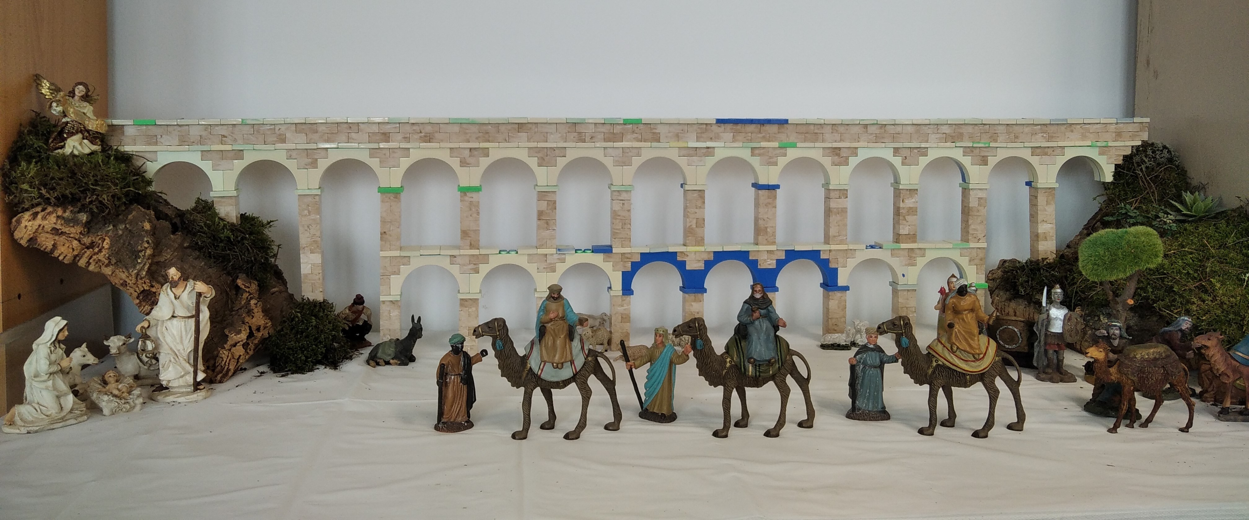 Pessebre amb figures tradicionals de Nadal disposades davant d’una gran recreació en 3D de l’aqüeducte romà de Tarraco. En primer terme hi ha el naixement amb Maria, Josep i el nen Jesús, diversos pastors i animals, així com els Reis d’Orient amb camells avançant pel centre de l’escena. Al fons, l’aqüeducte imprès en 3D, amb arcs successius de tons clars, actua com a escenografia principal, envoltat d’elements naturals com molsa i suro.