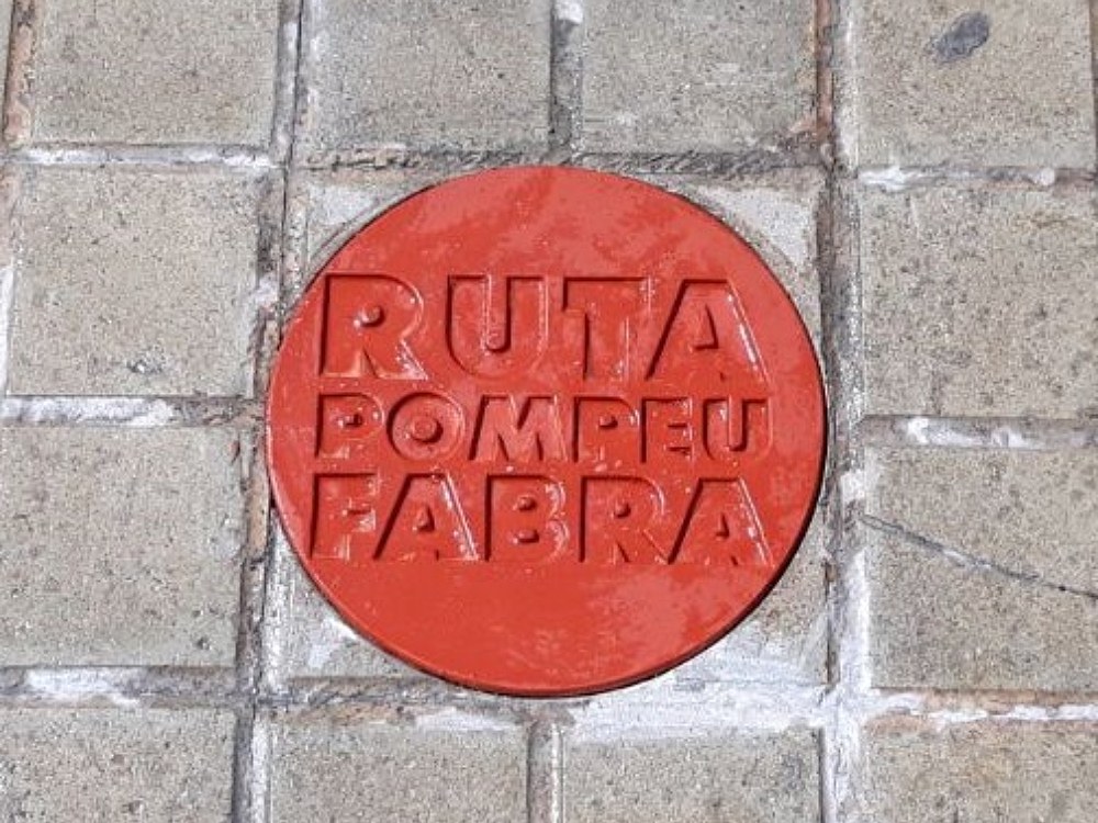Una rodona de color vermell amb les lletres "Ruta Pompeu Fabra" sobre unes llambordes.