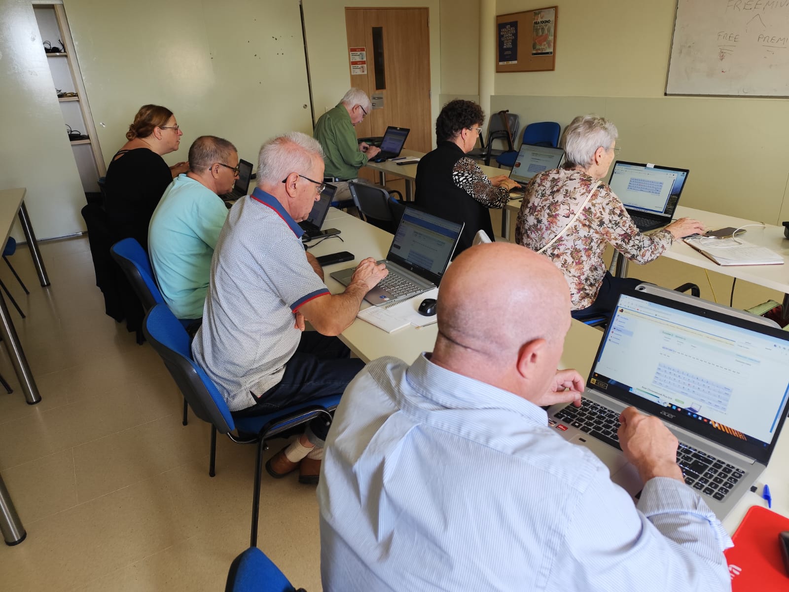 Un grup de persones participants del taller “Què puc fer jo per Palestina (a través d’Internet)” del Punt Òmnia de Santa Coloma de Cervelló treballant amb els seus ordinadors portàtils en una aula, centrades en la recerca i elaboració de recursos digitals.