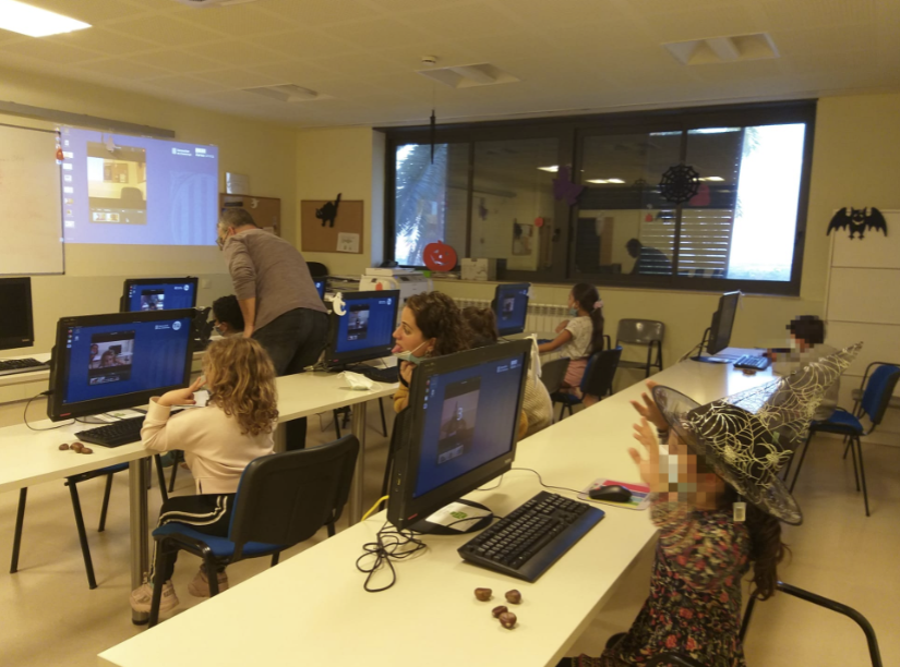 Grup de nens i nenes del Centre Obert La Klau treballant davant dels ordinadors al Punt Òmnia de Santa Coloma de Cervelló, amb el suport de la persona dinamitzadora. L’aula està decorada amb motius de Halloween i els infants participen en una activitat sobre ciberseguretat.