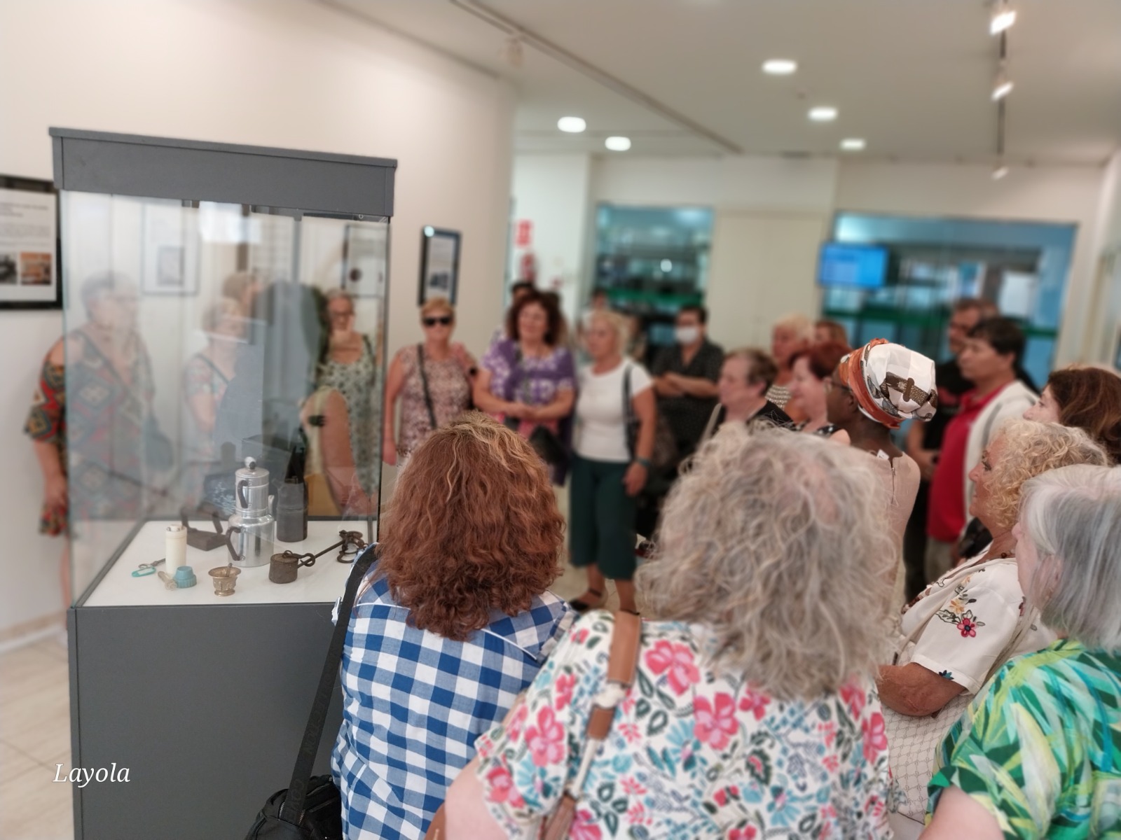 Un grup de veïnes i veïns del barri de la Torrassa observant amb atenció els objectes exposats en una vitrina durant la inauguració de l’exposició DomèsTIC al CCCT.