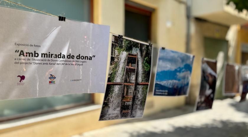 Imatge de l'exposició "Amb mirada de dona". Apareix un cartell amb el nom de l'exposició imprès i es veuen de fons algunes de les fotografies seleccionades.