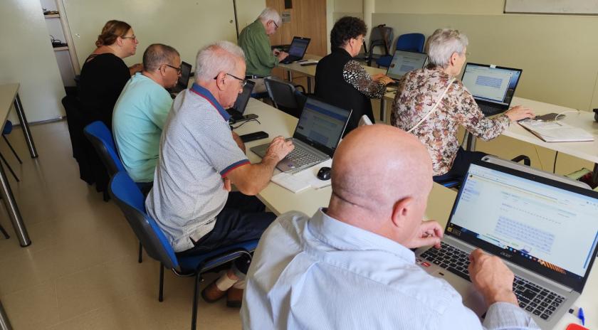 Un grup de persones participants del taller “Què puc fer jo per Palestina (a través d’Internet)” del Punt Òmnia de Santa Coloma de Cervelló treballant amb els seus ordinadors portàtils en una aula, centrades en la recerca i elaboració de recursos digitals.