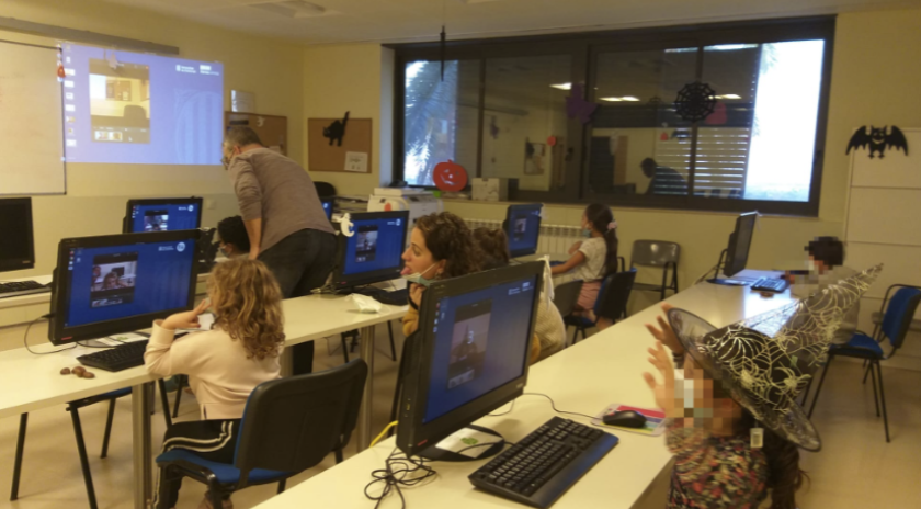 Grup de nens i nenes del Centre Obert La Klau treballant davant dels ordinadors al Punt Òmnia de Santa Coloma de Cervelló, amb el suport de la persona dinamitzadora. L’aula està decorada amb motius de Halloween i els infants participen en una activitat sobre ciberseguretat.