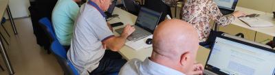 Un grup de persones participants del taller “Què puc fer jo per Palestina (a través d’Internet)” del Punt Òmnia de Santa Coloma de Cervelló treballant amb els seus ordinadors portàtils en una aula, centrades en la recerca i elaboració de recursos digitals.